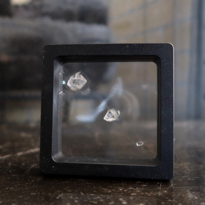 3 Double Terminated Raw Clear Quartz gemstones in zero gravity case on the floor