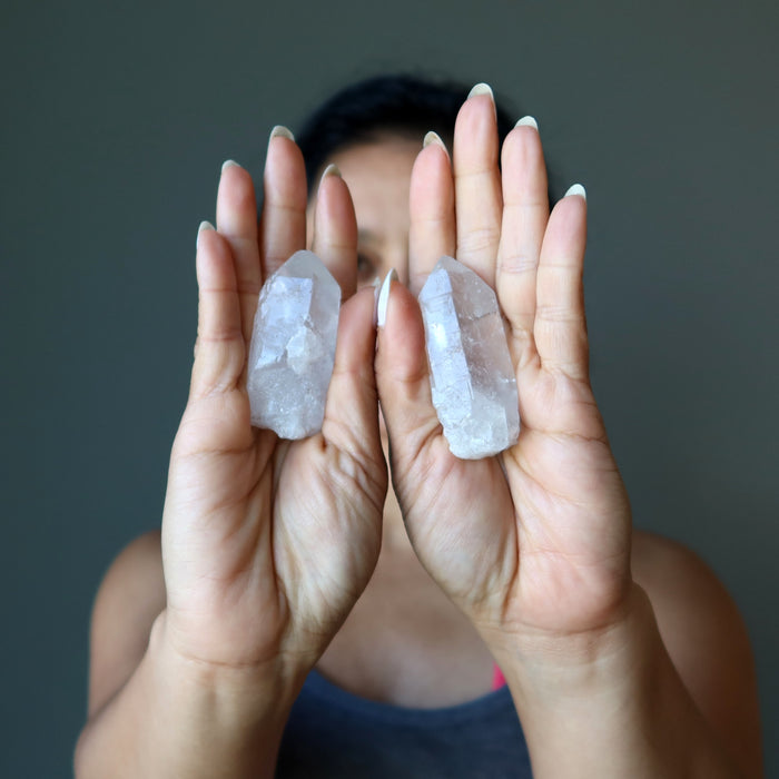 sheila of satin crystals holding two raw clear quartz points on each hand in front of her face
