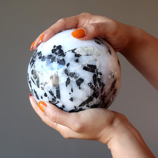 hands holding big tourmalined quartz sphere