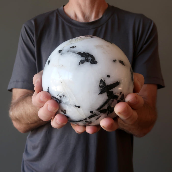 man's hands holding big tourmalined quartz sphere
