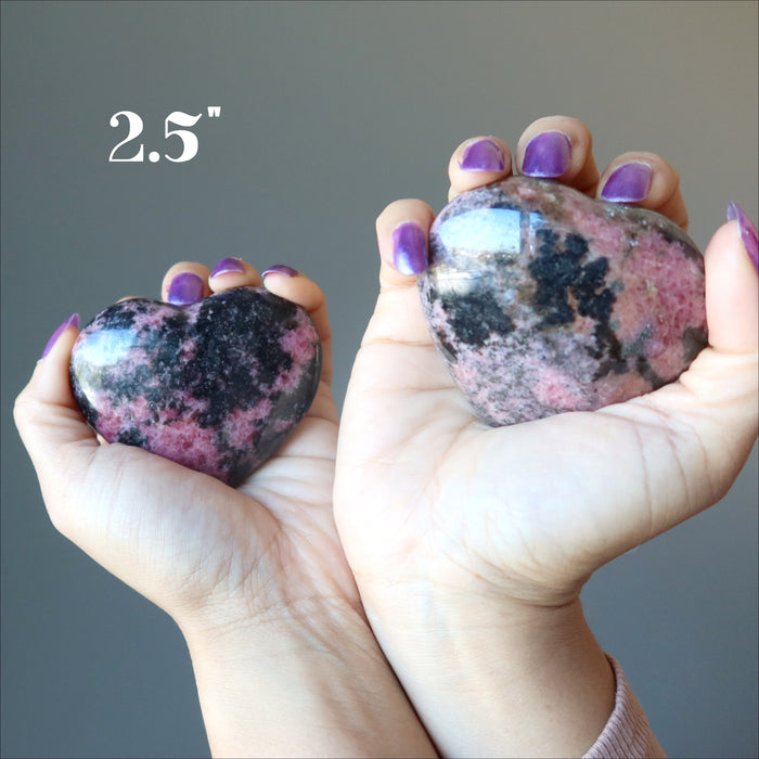 hands holding two rhodonite hearts