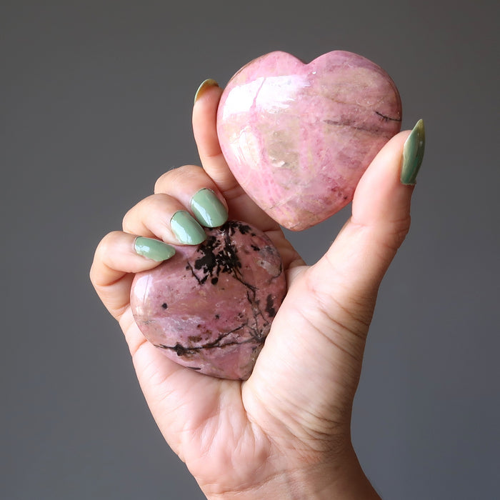 hand holding a pair of rhodonite hearts