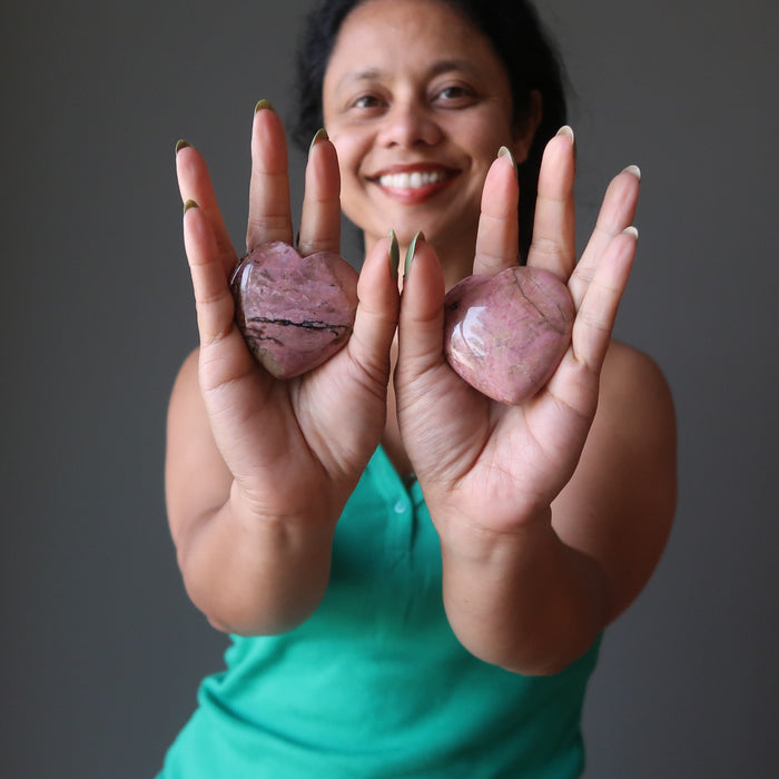 sheila of satin crystals holding up a pair of pink rhodonite hearts