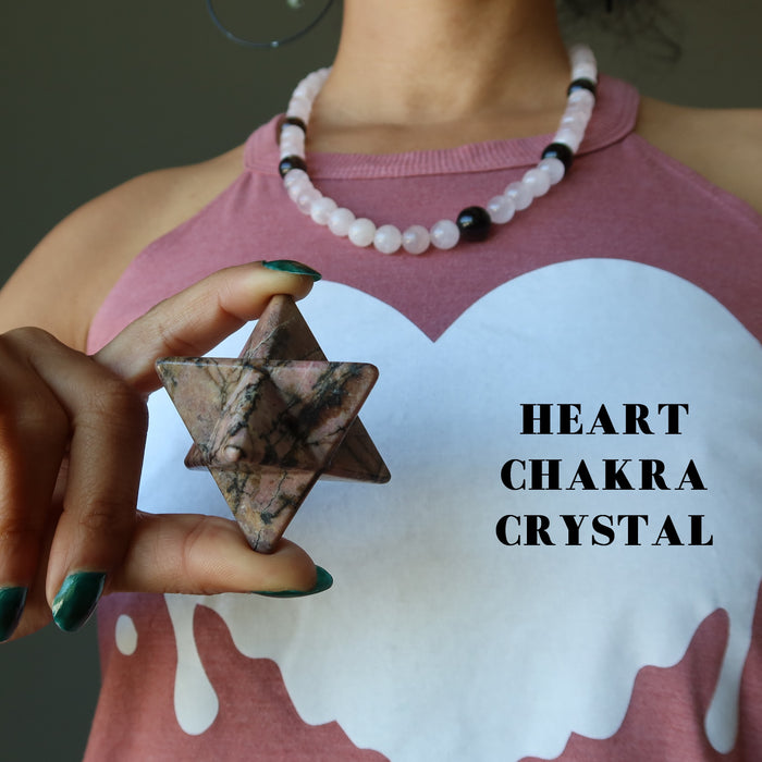hand holding pink and black rhodonite merkaba over the heart chakra