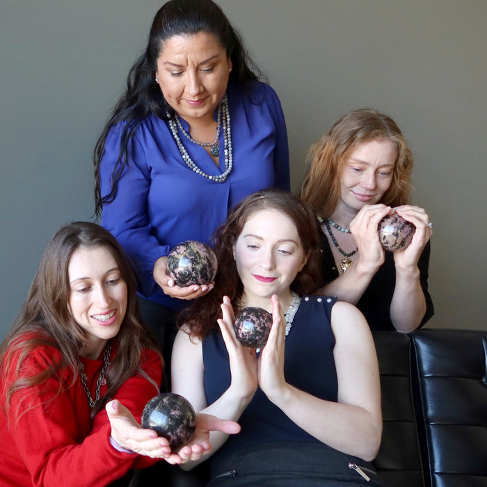 four women holding pink and black rhodonite spheres