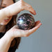 woman holding pink and black rhodonite sphere