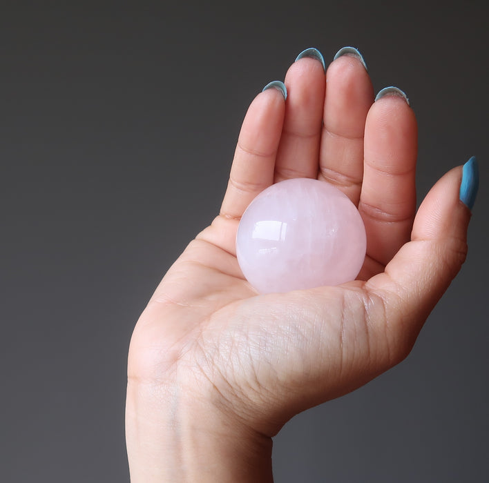 palm of hand holding pink rose quartz crystal ball