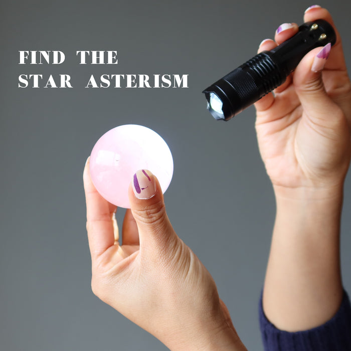 hands holding a flashlight up to a pink rose quartz sphere to find the star asterism