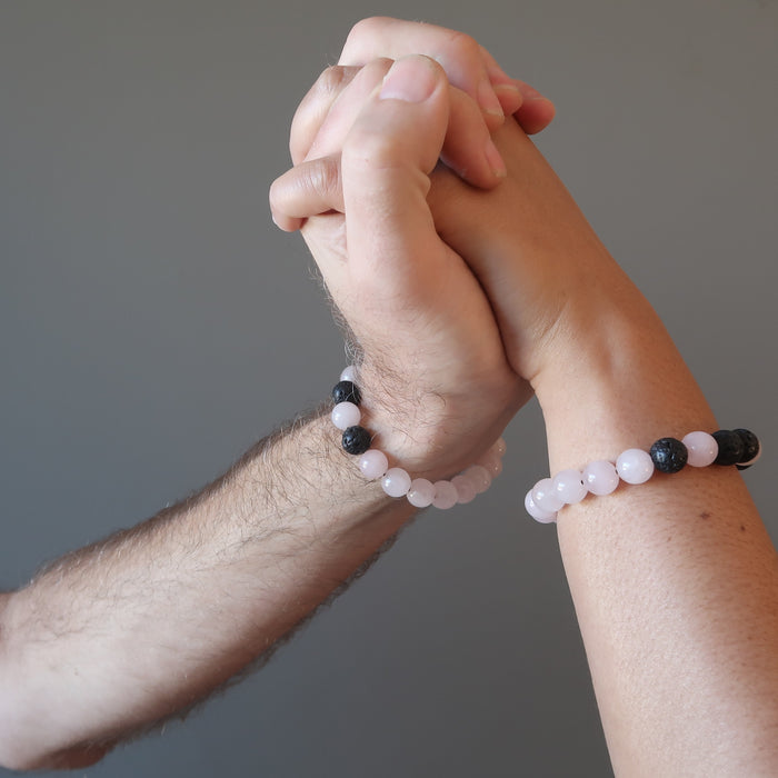 two rose quartz and black lava combo bracelets being modeled by a man's hand and a woman's hand