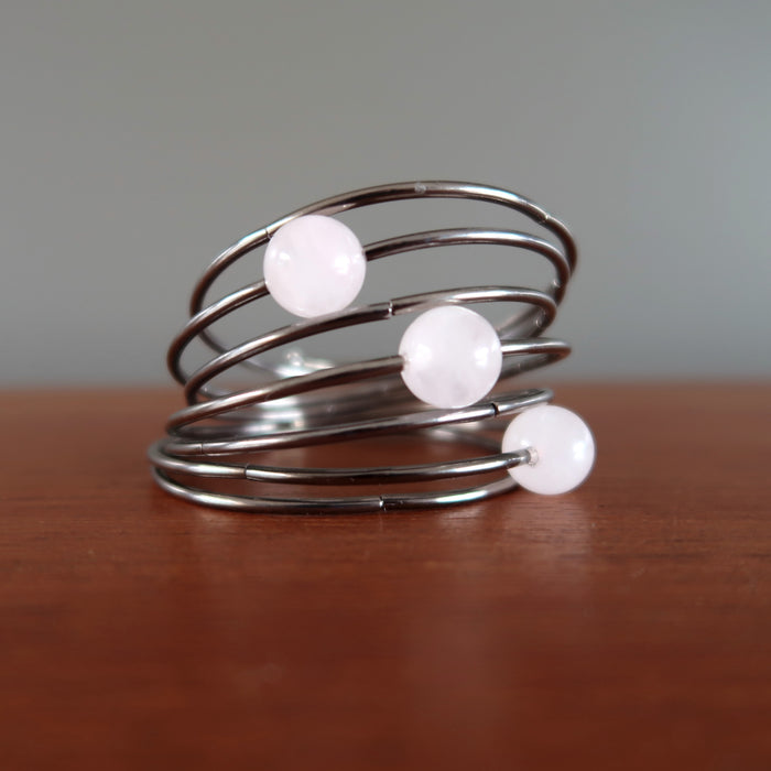 7 layer gunmetal coil bracelet with three statement beads in pink rose quartz displayed on wood desk