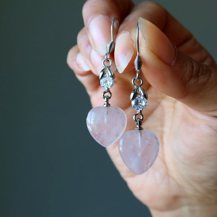 hands holding rose quartz heart earrings with sparkling crystal accents 