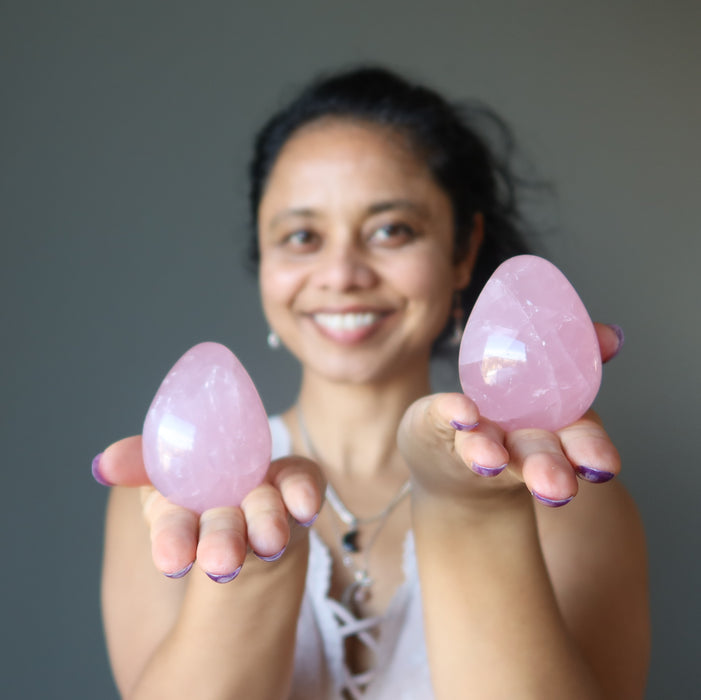woman holding two dark pink star rose quartz eggs