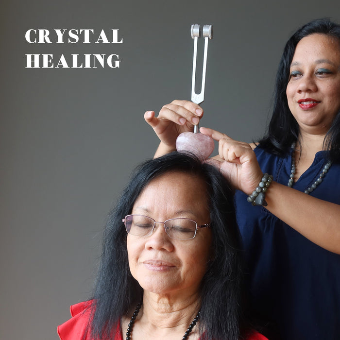 healer using a rose quartz heart and tuning fork on client's chakra