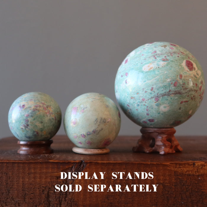 hand holding ruby fuchsite spheres on display stands
