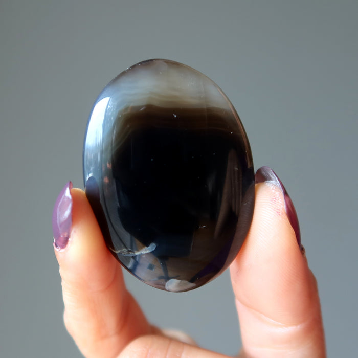 hand holding a black and brown sardonyx oval polished stone