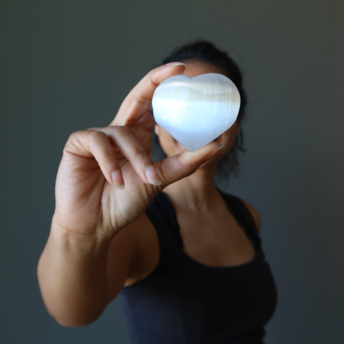 sheila of satin crystals holding a white selenite heart in front of her face