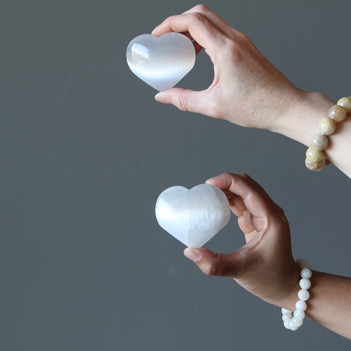 two hands each holding a selenite heart