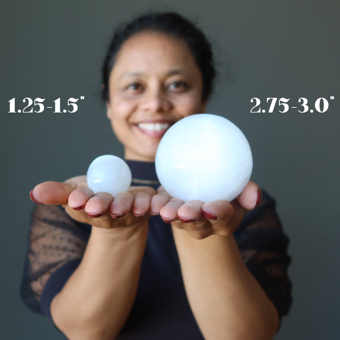 woman holding two white selenite sphere in different sizes
