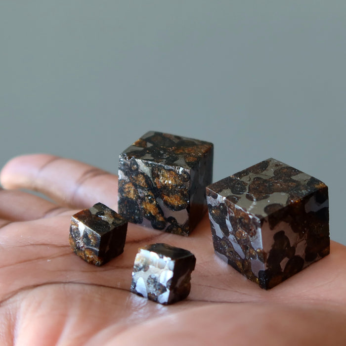 hand holding four silver and orange sericho meteorite cubes