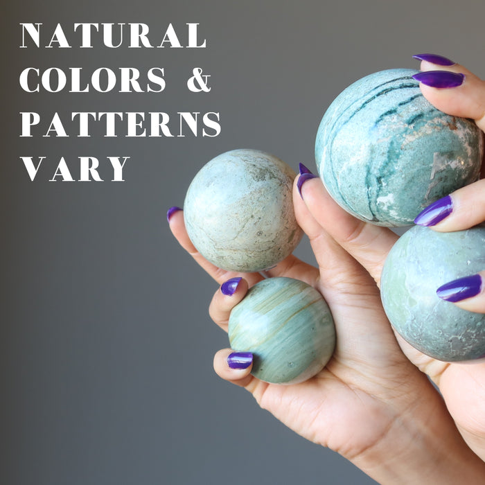 hands holding 4  serpentine spheres to show natural colors and patterns vary