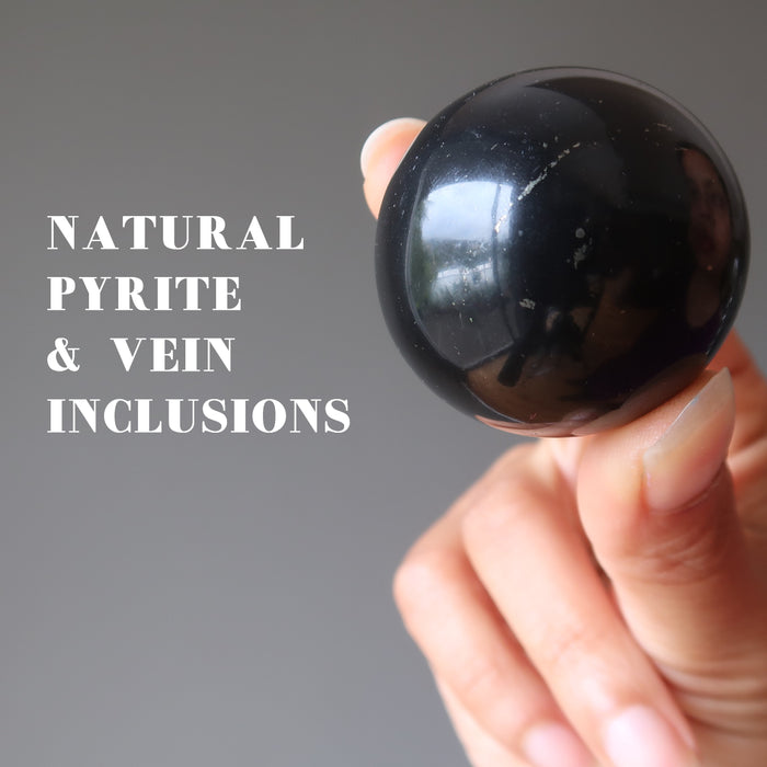 hand holding a shungite crystal sphere showing natural pyrite and vein inclusions