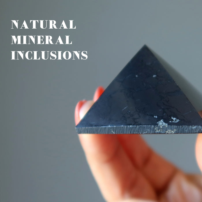 hand holding black shungite stone pyramid showing natural mineral inclusions