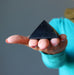 hand holding black shungite stone pyramid showing natural mineral inclusions