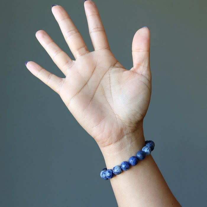 model raising hand wearing faceted round beaded sodalite bracelet on wrist