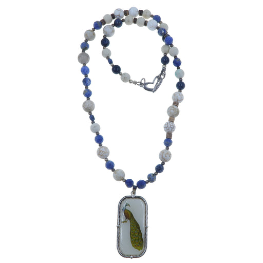 roundish, faceted, cubed Sodalite beads and white, brown Magnesite round beads strung with antiqued silver and brown coconut accent beads secured with a heart toggle clasp. The necklace features a rectangular metal pendant depicting a brilliant peacock.