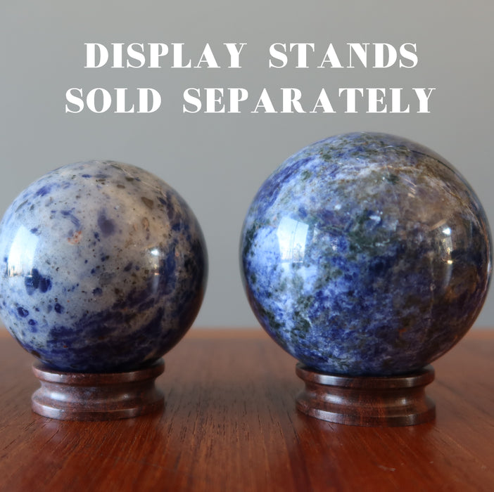 two hand holding blue sodalite spheres on wood display stands