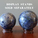 two hand holding blue sodalite spheres on wood display stands