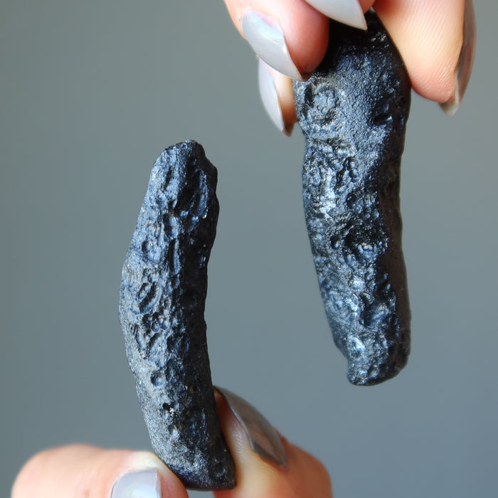hands holding rough black tektites