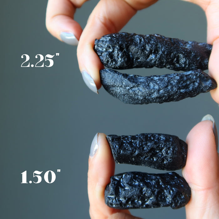 hands holding two sets of rough black tektites to show size difference