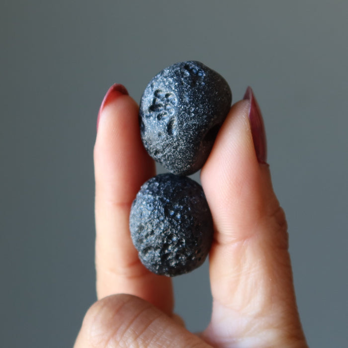 holding a pair of Two Round Black Tektite Meteorites 