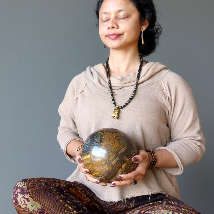 sheila of satin crystals meditating with a giant brown tigers eye sphere with veins of black hematite