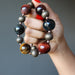 hand holding golden, blue and red tigers eye on antiqued beaded necklace