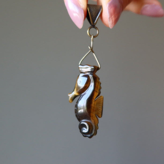 hand holding golden brown tigers eye seahorse pendant