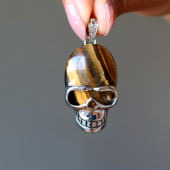 hand holding golden brown tigers eye in aviator skull pendant 