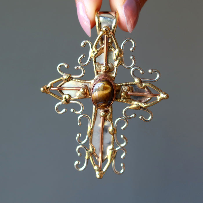 hand holding golden tigers eye oval in fancy metal cross pendant