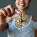 sheila of satin crystals holding golden tigers eye oval in fancy metal cross pendant