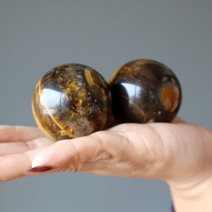 on palm displaying 2 Den Muddy Earth Tigers Eye Sphere