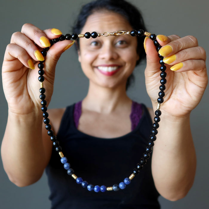 sheila of satin crystals holding up a faceted black tourmaline and blue sodalite necklace