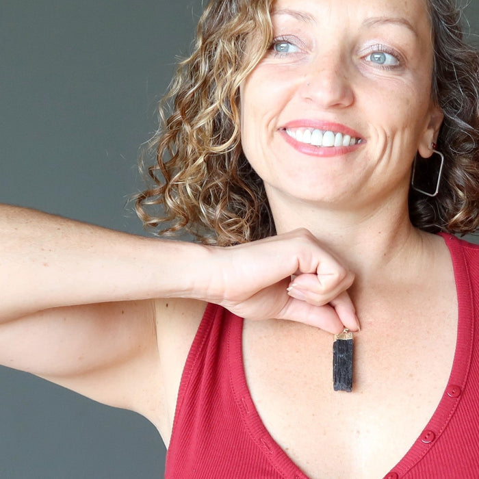 woman holding raw black tourmaline on gold electroplated pendant to her chest