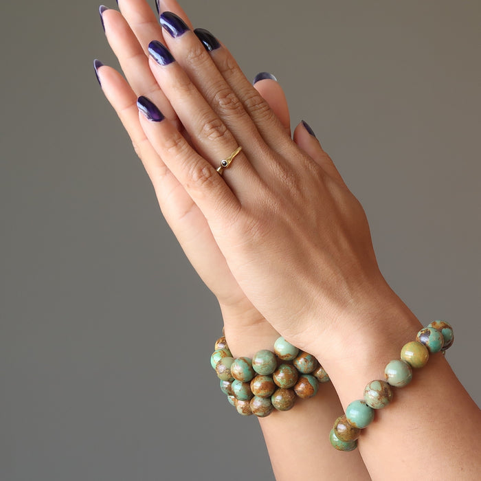hands clasped wearing 4 green and brown turquoise jasper round beaded stretch bracelet