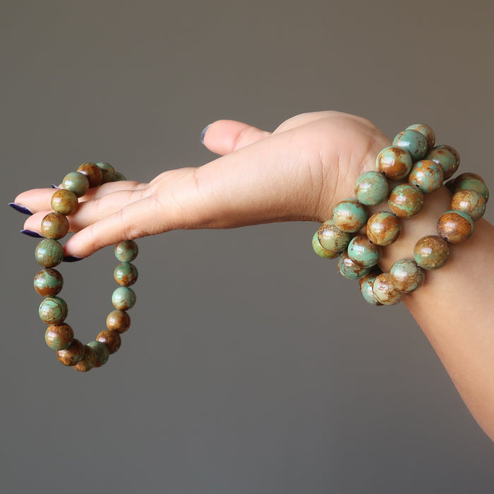 hand wearing and holding green and brown turquoise jasper round beaded stretch bracelets