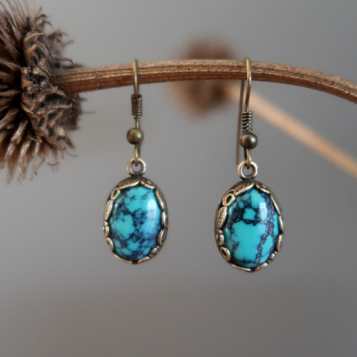 a pair of Blue Oval Antiqued Leaf Turquoise Earrings hanging on the dry brown branch