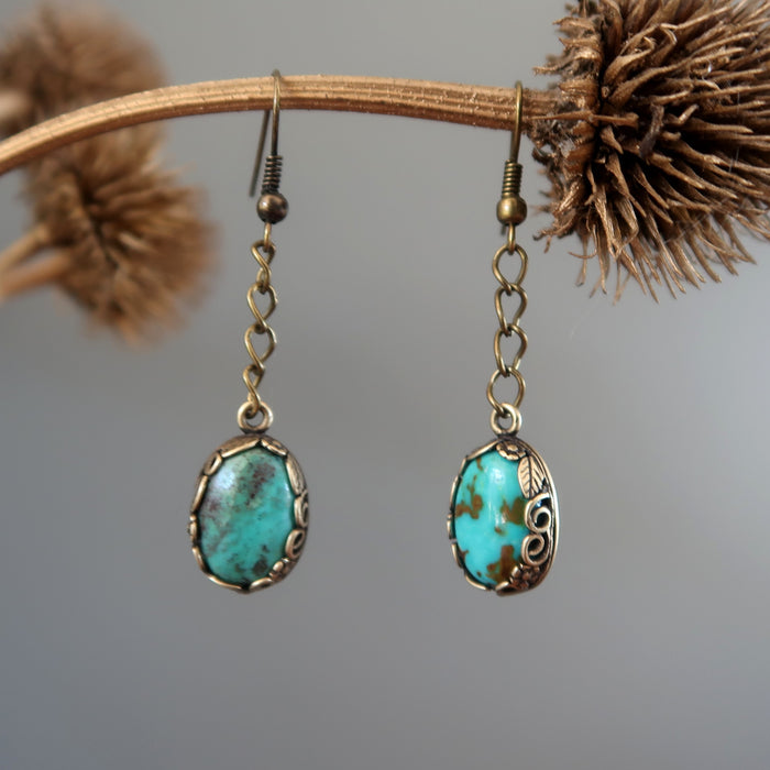 a pair of Blue Oval Antiqued Leaf Turquoise Earrings hanging on the dry brown branch