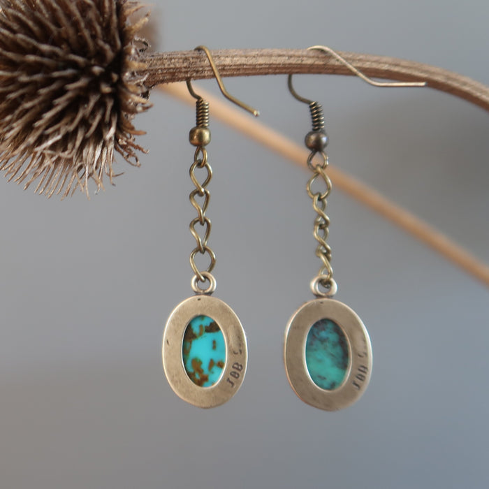 back of a pair of Blue Oval Antiqued Leaf Turquoise Earrings hanging on the dry brown branch